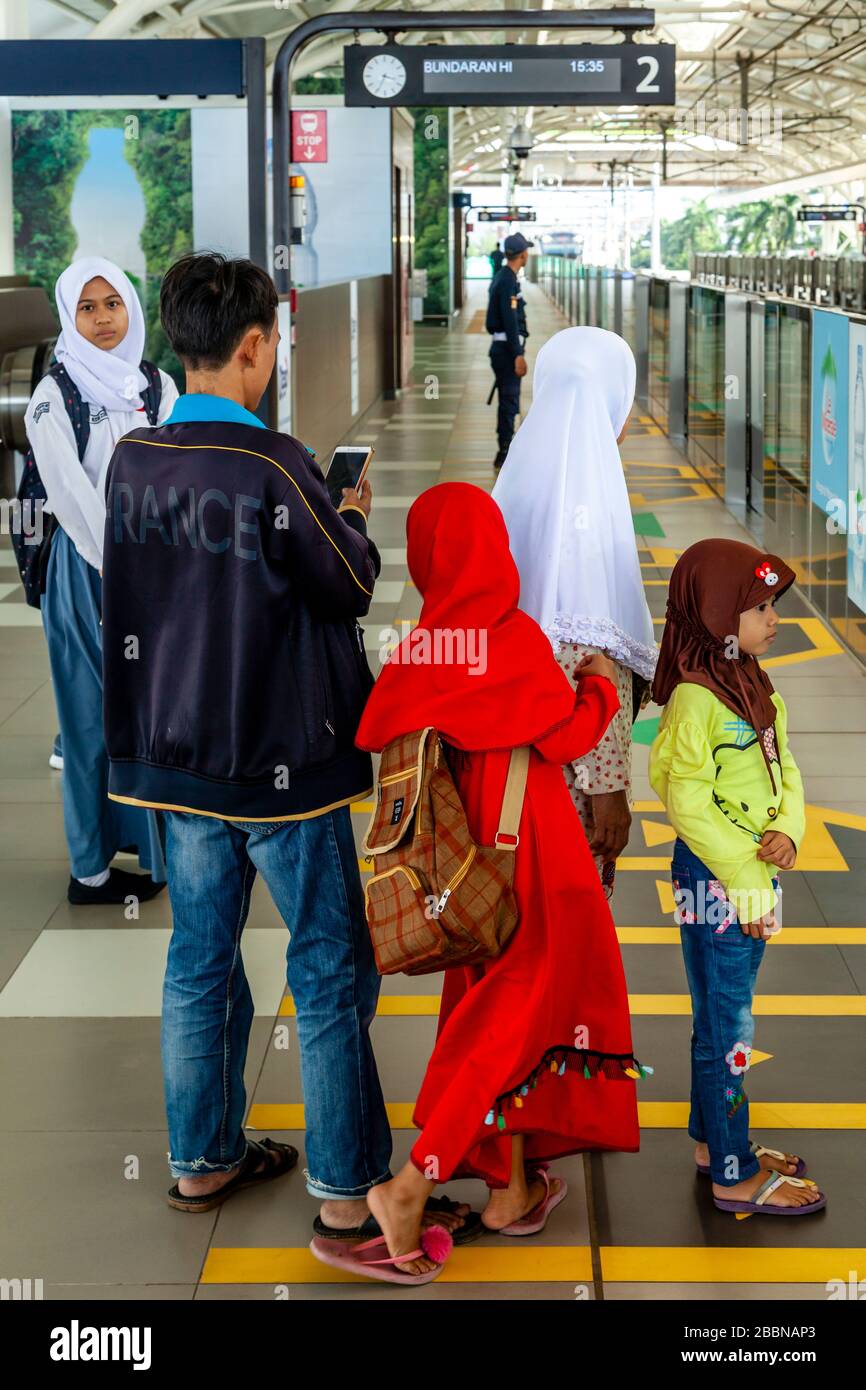 Une famille indonésienne attend sur la plate-forme de la gare comme un train approche, le métro (MRT), Jakarta, Indonésie. Banque D'Images