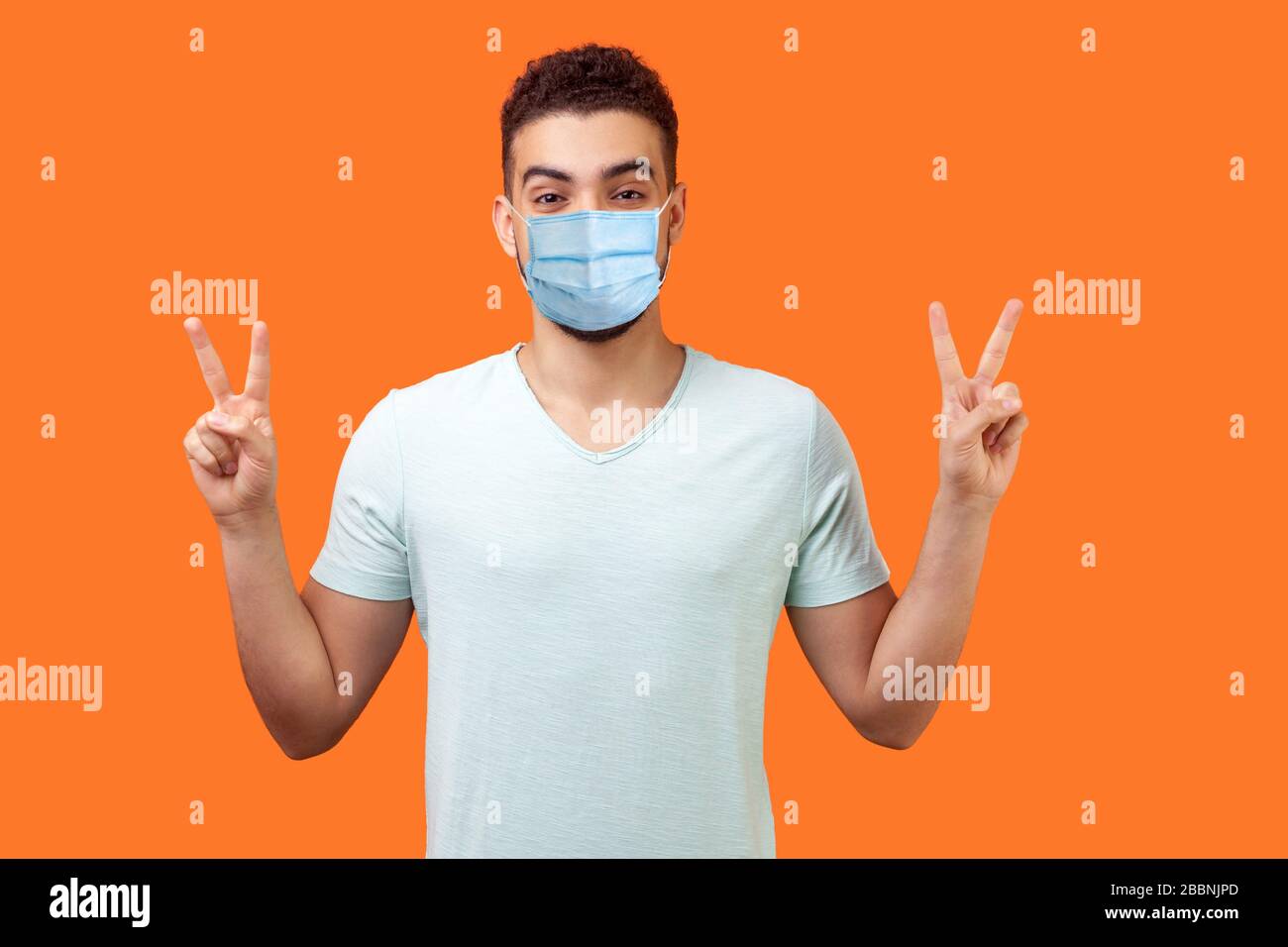 Victoire ! Portrait de heureux homme de brunette réussi avec masque médical chirurgical souriant heureux et montrant deux v signe ou geste de paix, se réjouissant gagner. i Banque D'Images
