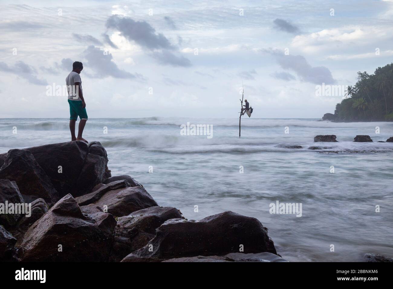 Pêche aux pêcheurs de stilt alors qu'un garçon regarde sur la rive de la plage de Mirissa sur la côte sud du Sri Lanka Banque D'Images