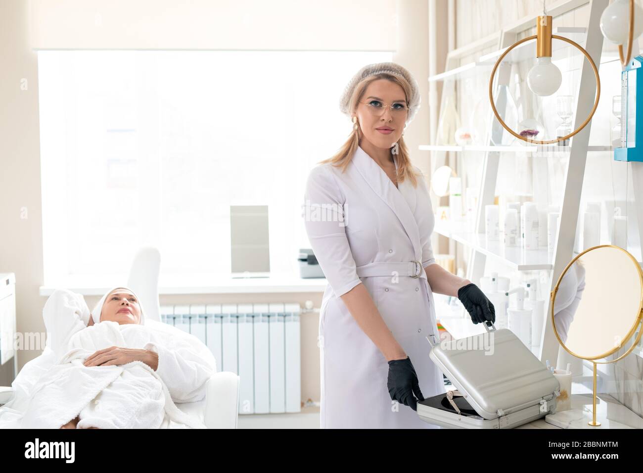 Portrait du jeune cosmologiste dans une capsule chirurgicale et des gants ouvrant la valise de produits cosmétiques pendant la préparation de la procédure Banque D'Images