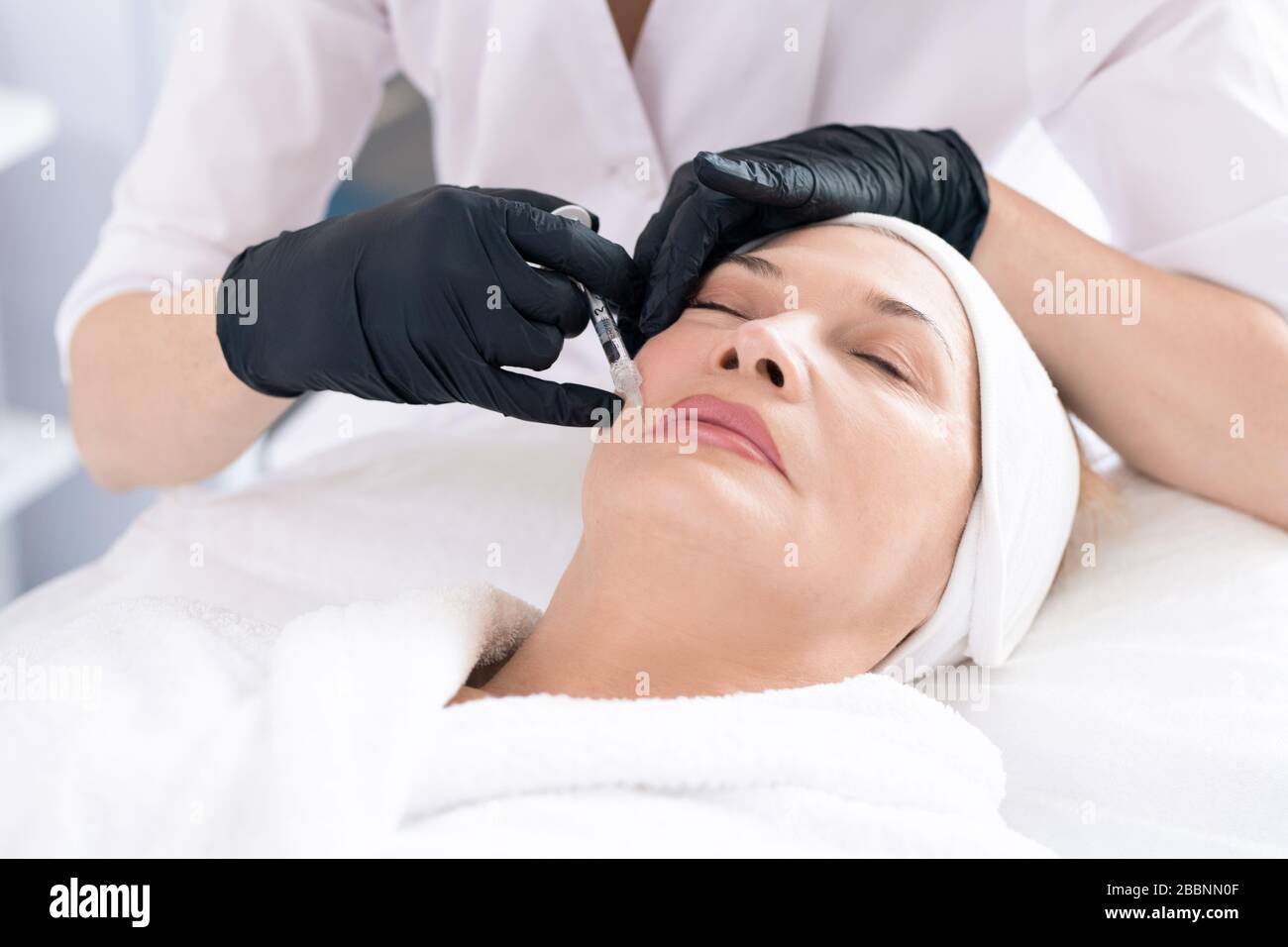 Gros plan du cosmologiste dans les gants chirurgicaux injectant du mastic au client tout en éliminant les rides autour de la bouche Banque D'Images