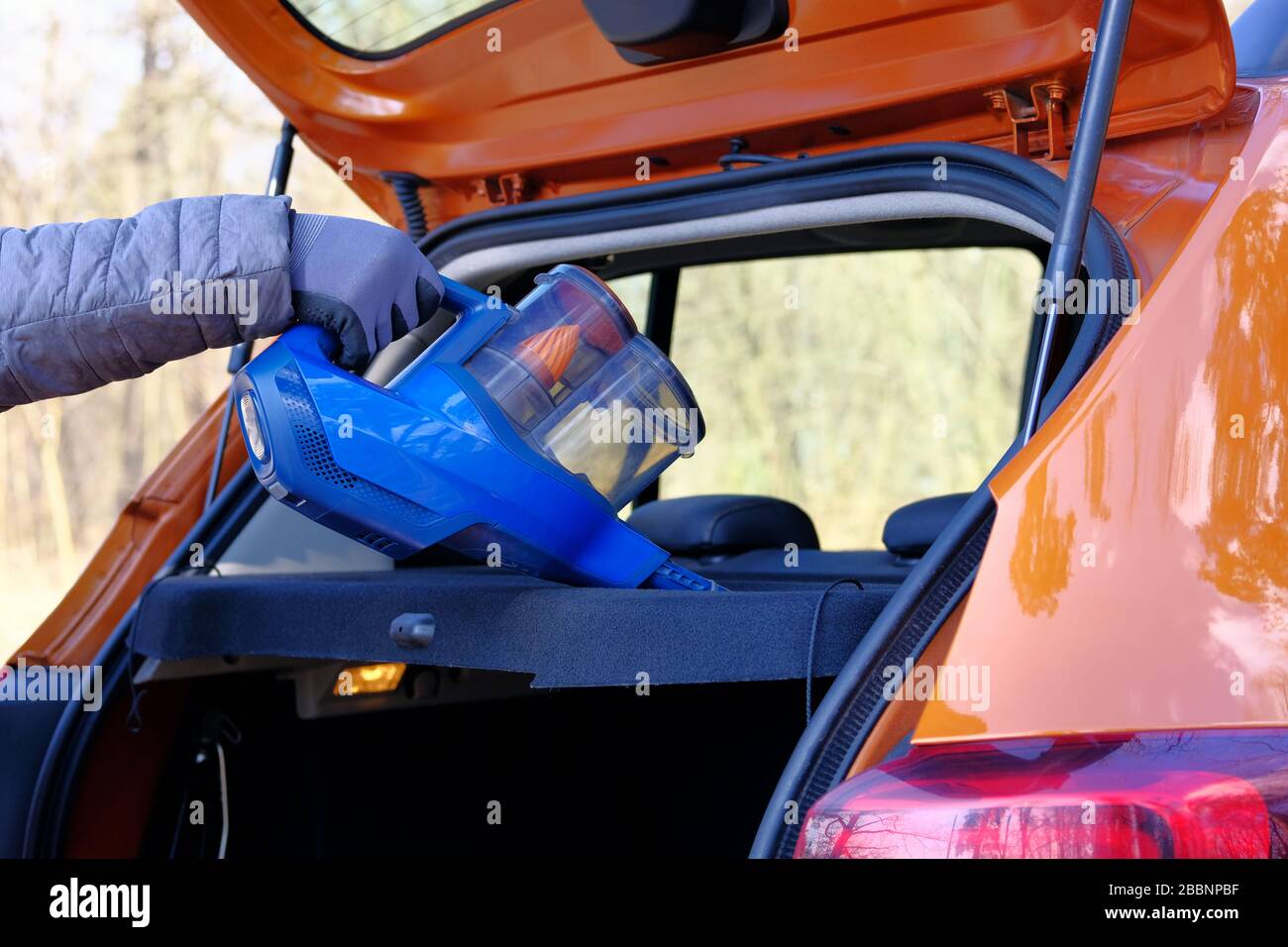 Aspirateur entre les mains du conducteur de voiture. Nettoyage du coffre de l'automobile avec aspirateur bleu, gros plan. La voiture est régulièrement nettoyée. Banque D'Images