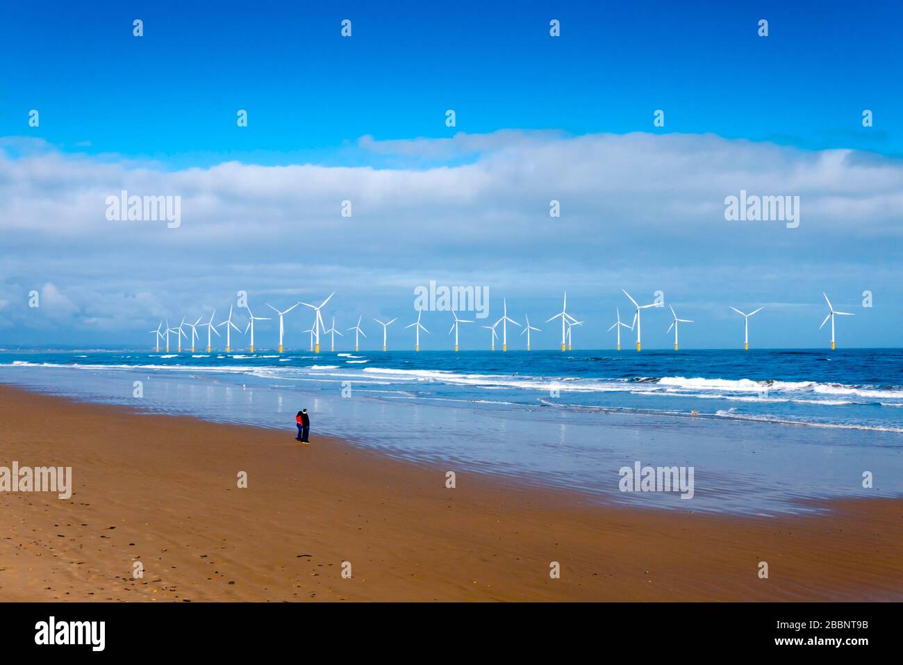 Parc éolien Redcar éclairé par le soleil depuis la plage avec les 27 éoliennes présentées avec un couple et un chien Banque D'Images