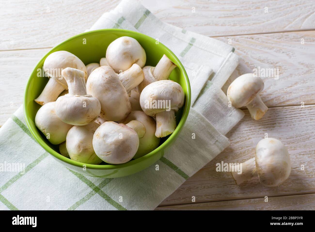Champagnes frais crus entiers dans un bol vert sur une serviette de cuisine au-dessus d'une table en bois. Champignons en tant que protéines végétales, alimentation alimentaire brute, végétarisme. Banque D'Images
