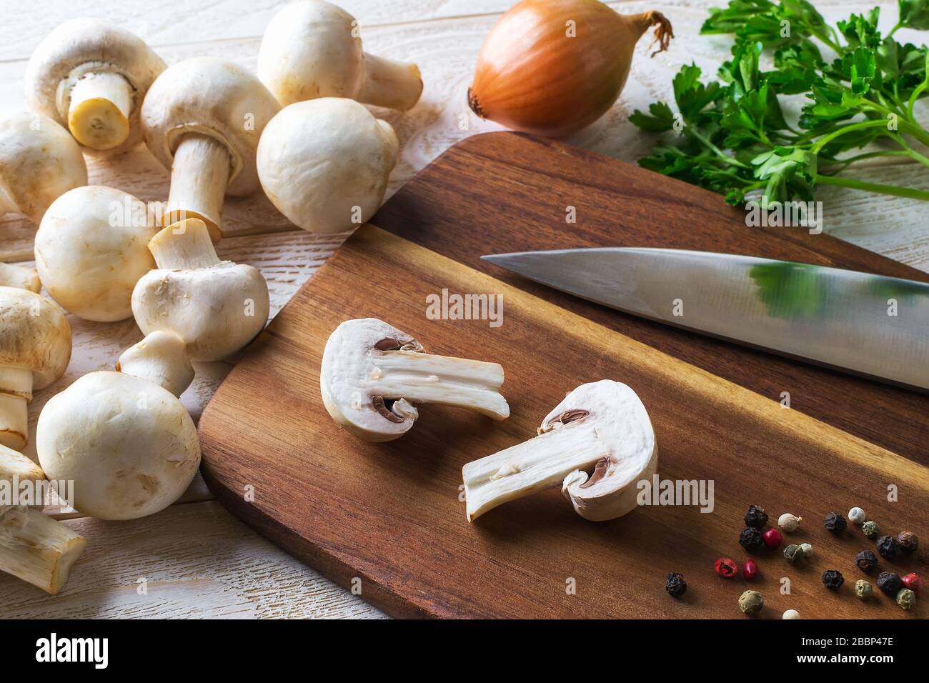 Champignon avec deux branches et couteau sur un tableau de découpe près de tas de champignons crus, d'oignons et de persil. Champignons en tant que protéines végétales, alimentation alimentaire brute. Banque D'Images