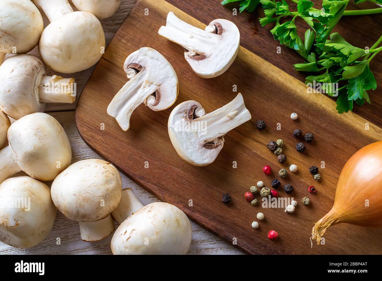 Trois moitiés de champagnes, de poivre, d'oignon et de persil sur une planche à découper en bois. Champignons en tant que protéines végétales, alimentation alimentaire brute, végétarisme. Banque D'Images