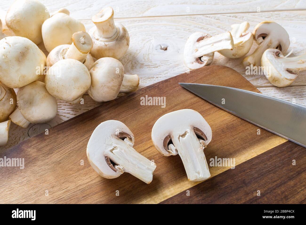 Champignon avec deux coupes et couteau sur une planche à découper près d'un tas de champignons frais crus sur une table en bois. Champignons en tant que protéines végétales, alimentation alimentaire brute. Banque D'Images