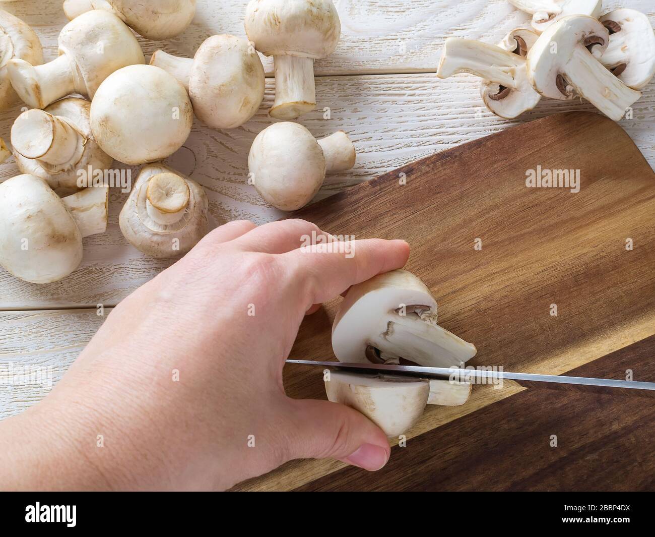 Femme tenant une main de chamignon avec un couteau tranchant sur une planche à découper en bois. Champignons en tant que protéines végétales, alimentation alimentaire brute, végétarisme. Banque D'Images