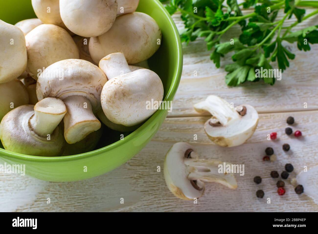 Champagnes frais crus entiers dans un bol vert près d'un bouquet de persil sur une table en bois. Champignons en tant que protéines végétales, alimentation alimentaire brute, végétarisme. Banque D'Images