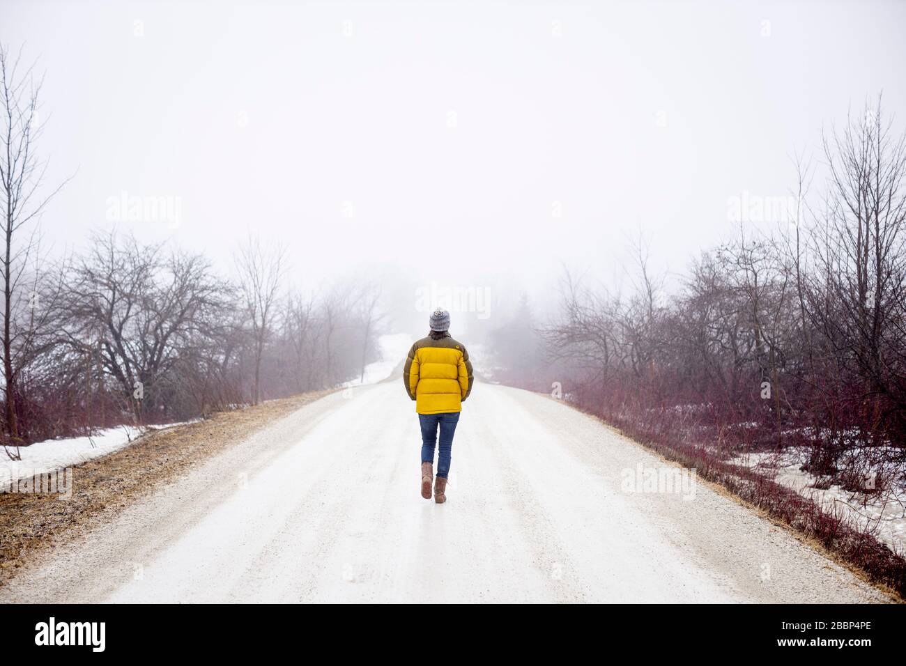 Une dame marche seule sur une route de gravier pendant la réglementation d'urgence concernant le coronavirus / COVID-19, sur une journée de printemps froid brumeuse. --- Banque D'Images