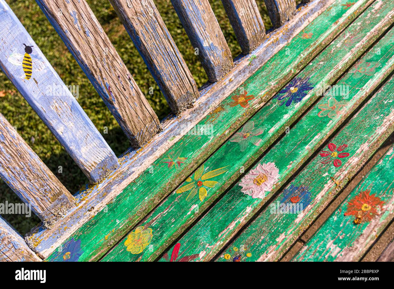 Banc coloré peint à la main et résisté à l'eau ou banc de parc avec fleurs, pétales et abeilles de différentes couleurs se forment dans une zone verte urbaine Banque D'Images