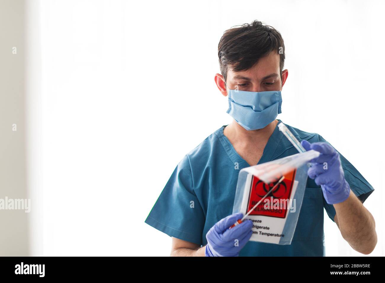 Le technologue en santé médicale qui tient le kit de collecte d'écouvillons COVID 19, porte un masque de protection blanc et des gants Banque D'Images