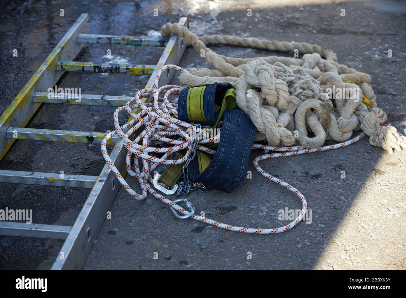 L'équipement composé d'une échelle, de cordes et d'une ceinture de sécurité pour travailler à haute altitude se trouve sur l'asphalte. Banque D'Images