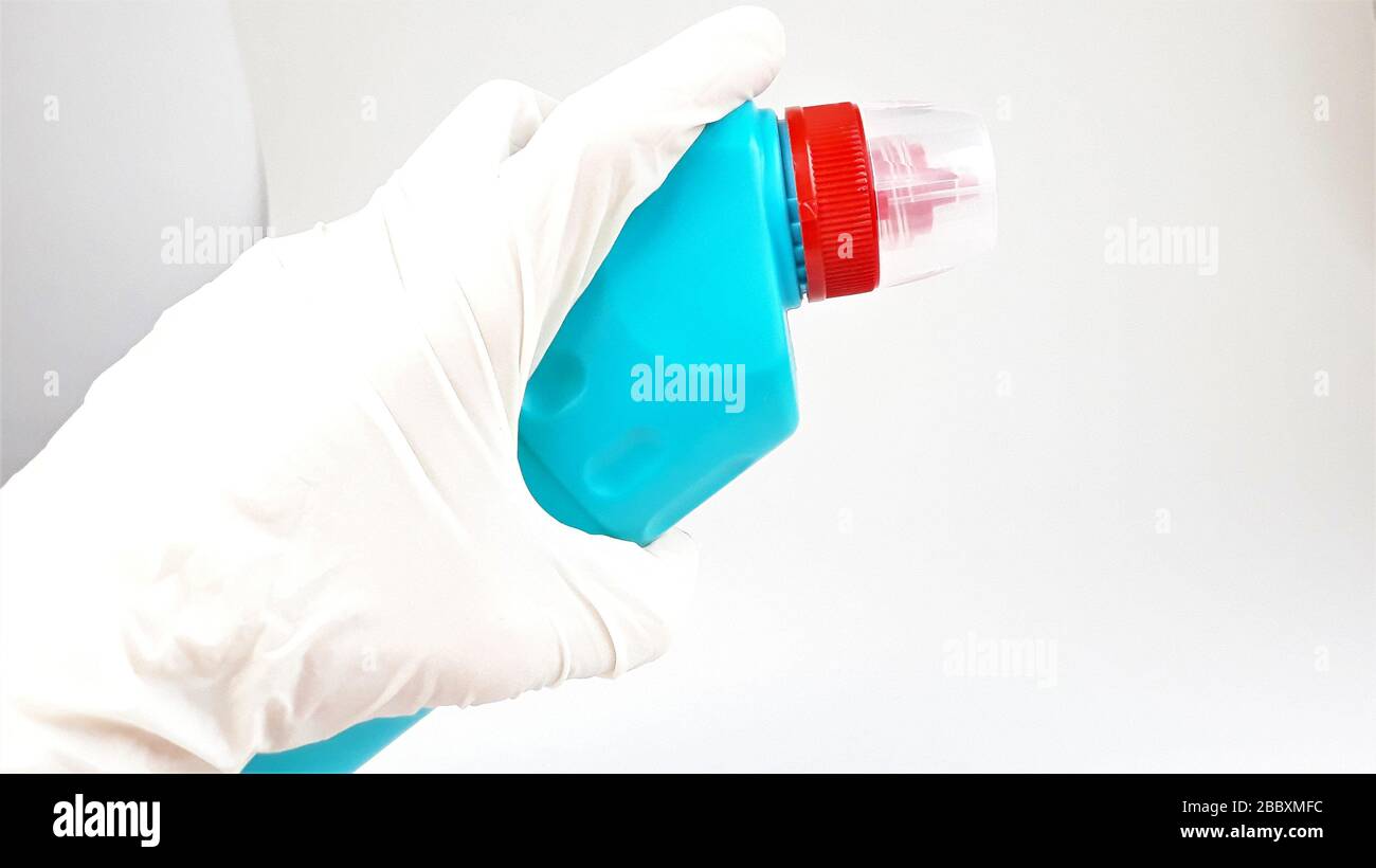 Bouteille en plastique bleu avec capuchon rouge à la main dans un gant blanc en caoutchouc sur fond blanc.liquide pour le nettoyage et la désinfection des chambres et des maisons. Banque D'Images
