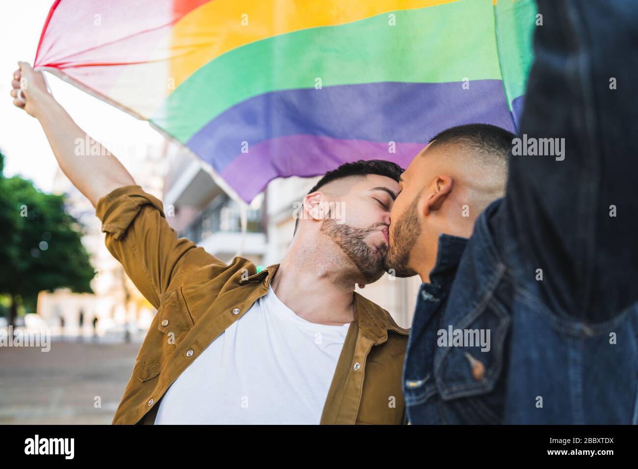 Portrait of young couple embracing et montrant leur amour avec drapeau arc-en-ciel à la rue. Amour LGBT et concept. Banque D'Images