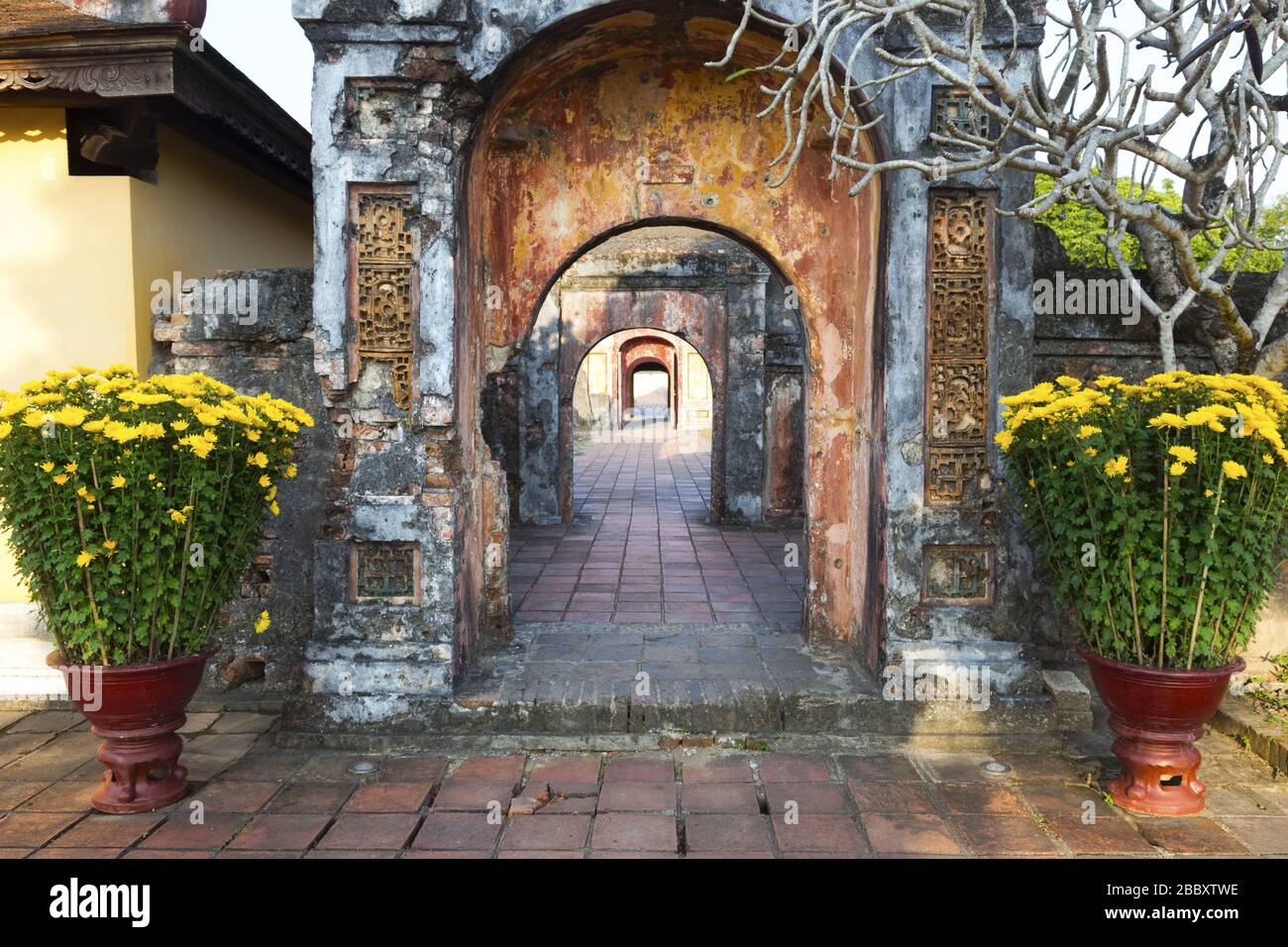 Couloir ancien avec murs de briques et portails éloignés avec fleurs jaunes dans un Flowerpot. Hue Imperial Palace Cité interdite, Vietnam Asie Banque D'Images