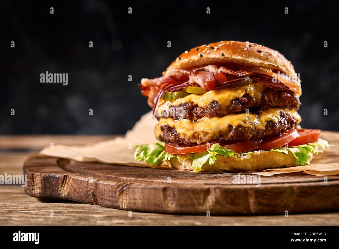 Hamburger américain juteux, hamburger ou cheeseburger avec deux viandes de bœuf, sauce et sur fond noir. Concept de restauration rapide américaine Banque D'Images