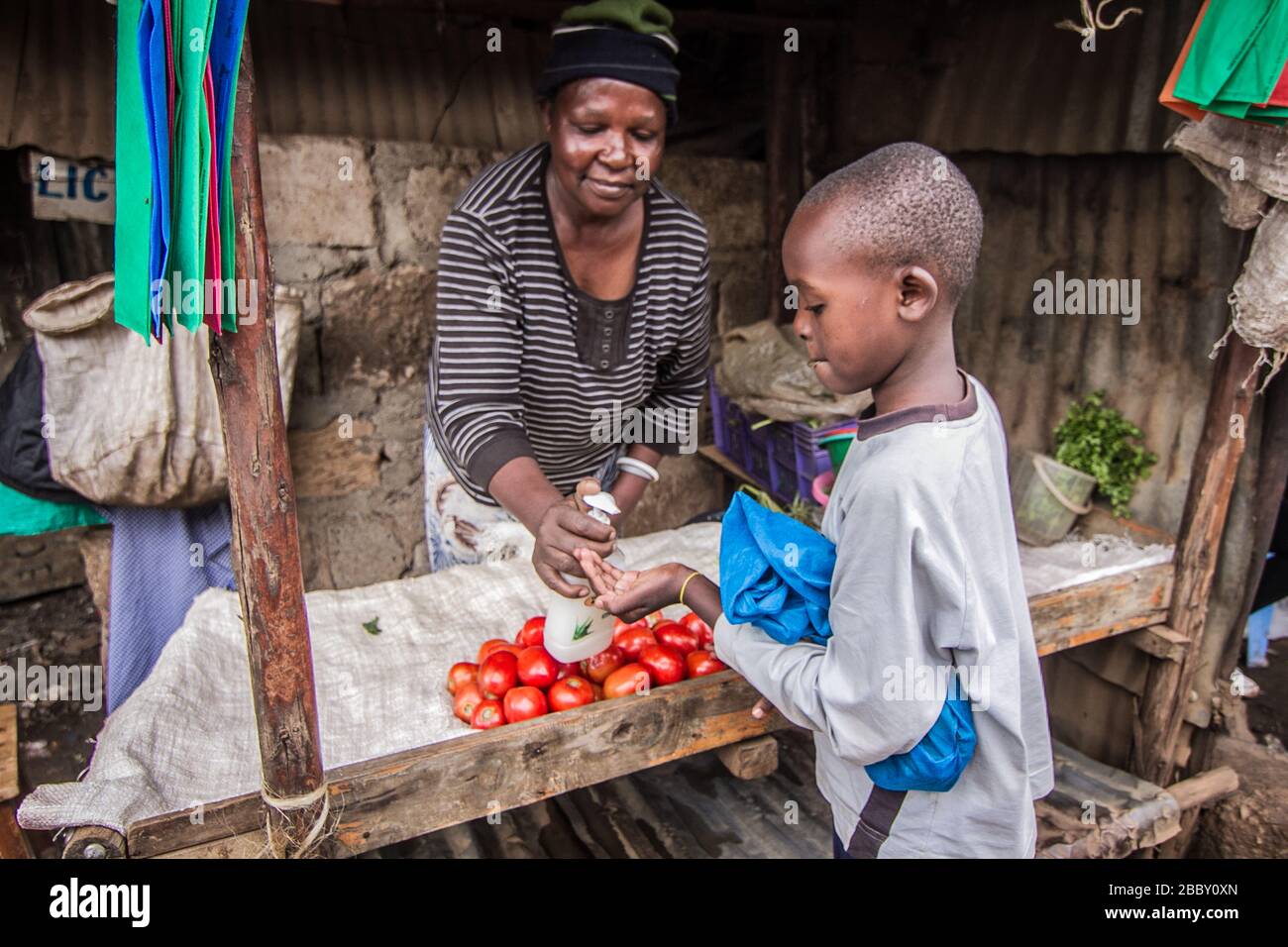 Hellen Mong'ina, une femme d'affaires de 58 ans de Kibera, désinfecte les mains de son jeune client pendant le couvre-feu.A la suite de la pandémie du virus corona, Le gouvernement du Kenya a imposé un couvre-feu qui a rendu beaucoup moins de revenus et a fait remonter la crise alimentaire qui oblige beaucoup des communautés pauvres à sortir sans aucune protection contre leur santé. Banque D'Images