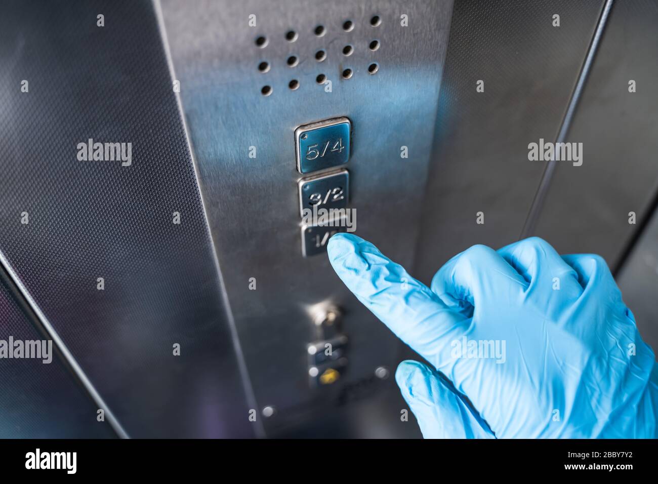 Homme utilisant des gants pour appuyer sur le bouton pour se protéger de l'infection par le coronavirus Banque D'Images