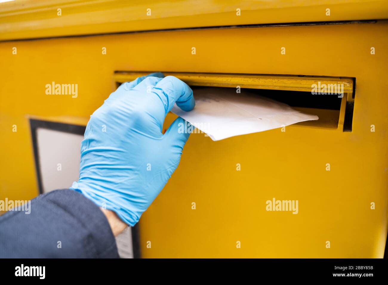 Homme Insertion de lettre dans la boîte aux lettres portant des gants pour protéger contre le Coronavirus Banque D'Images