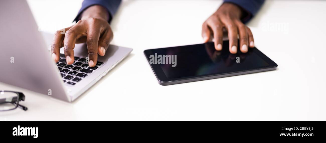 Les mains d'un homme d'affaires utilisant une tablette et un ordinateur portable sur le bureau Banque D'Images