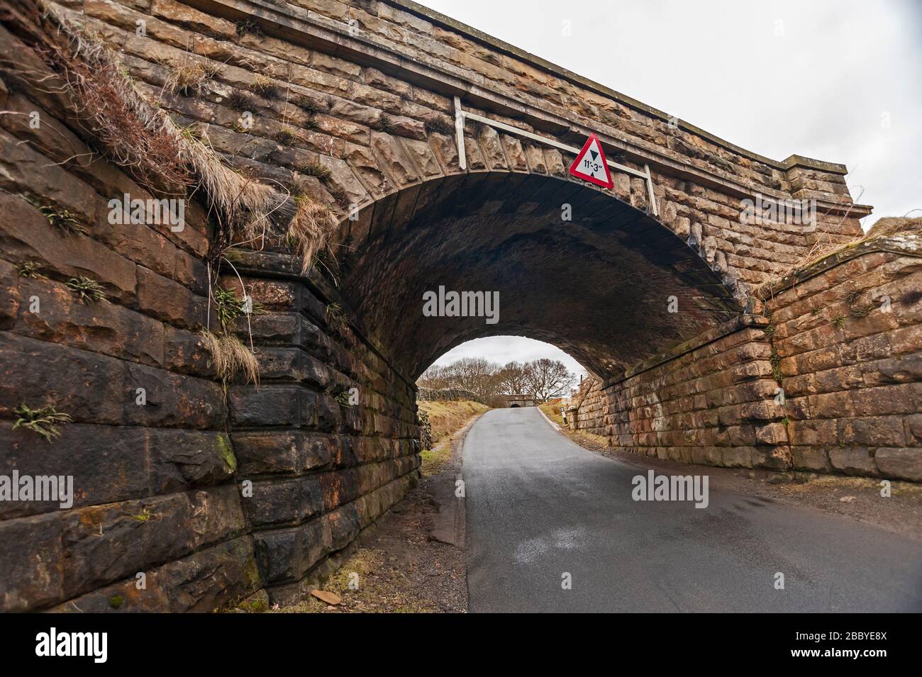 Vieux pont de chemin de fer en pierre avec de faibles signes d'avertissement sur un chemin de campagne Banque D'Images