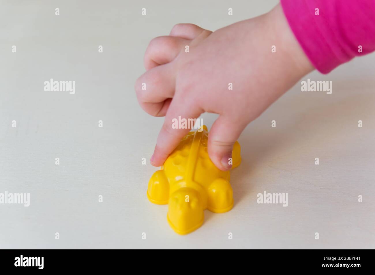 Mains de l'enfant tenant le petit jouet sur le fond de bois. Tortue jaune en plastique dans les mains de l'enfant. Banque D'Images