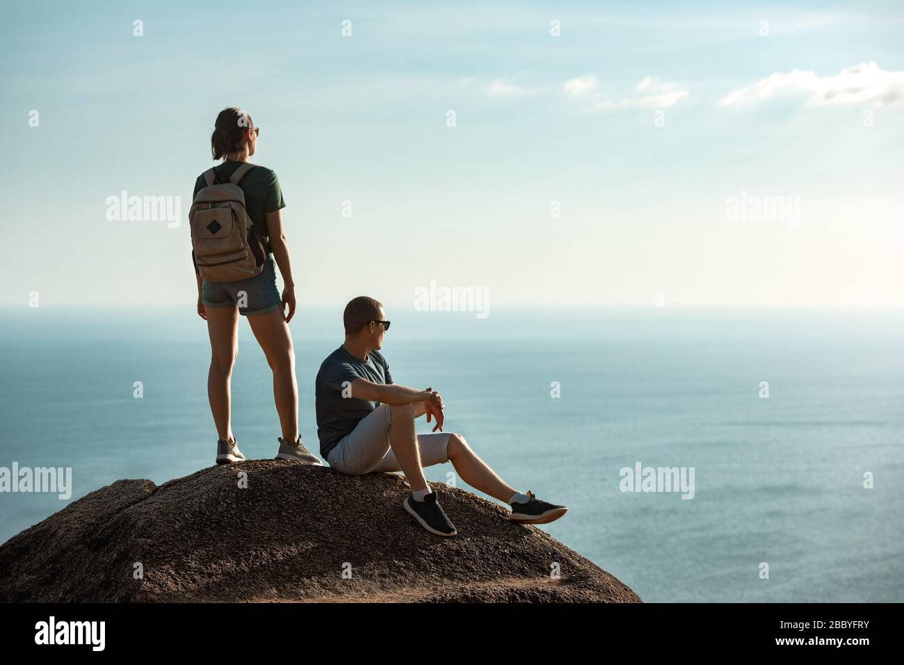 Deux jeunes randonneurs se détendant sur de grands rochers contre la mer et le ciel Banque D'Images