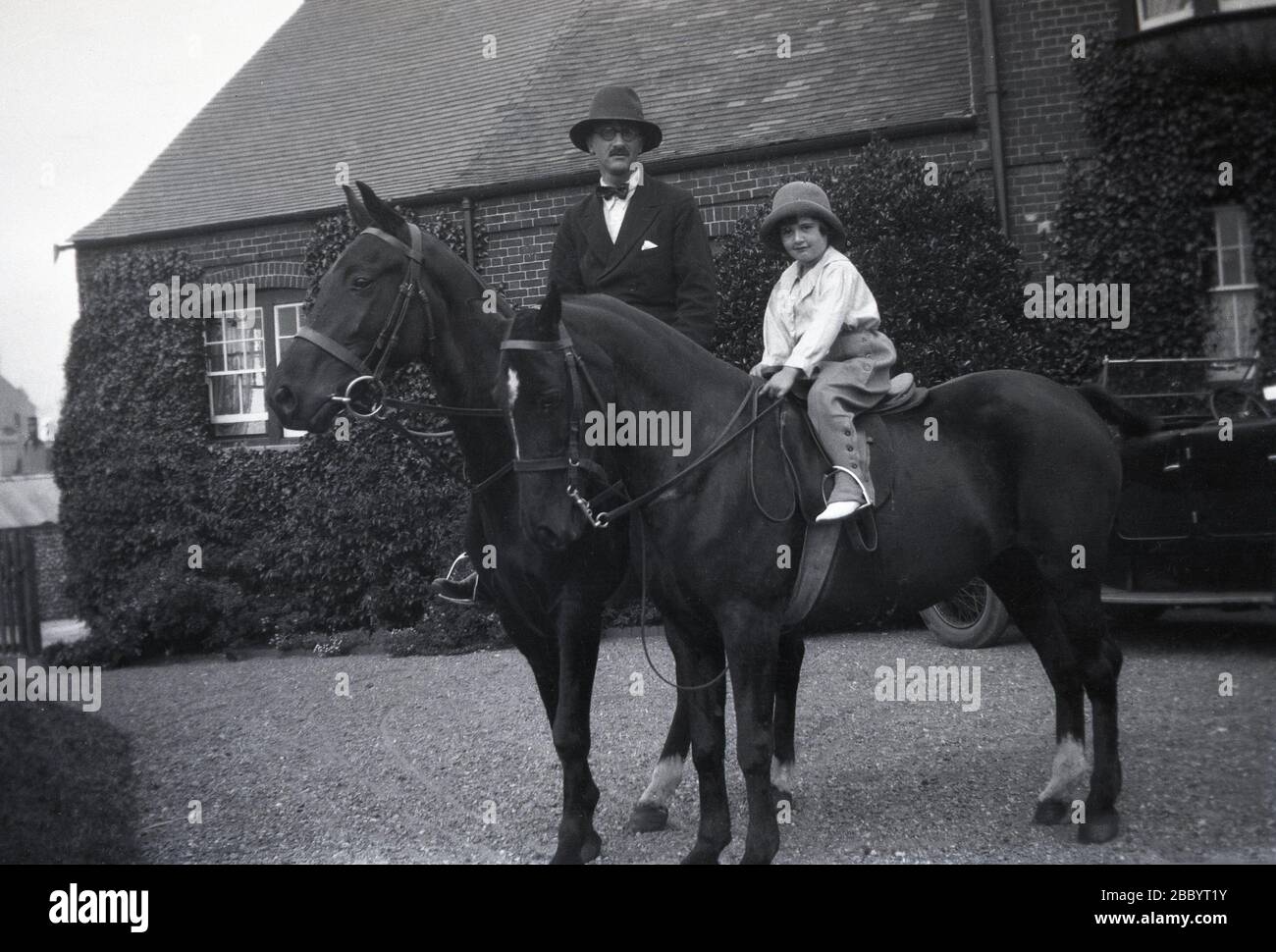 1920, un père et sa jeune fille assis sur leurs chevaux sur le gravier  l'allée d'une grande maison de campagne, Angleterre, Royaume-Uni. Le  gentleman porte les vêtements officiels de l'époque, un costume,