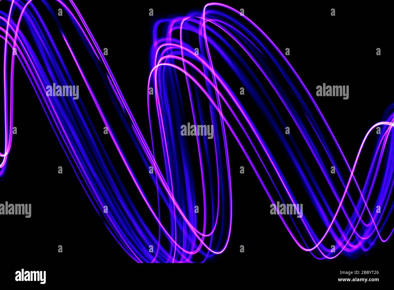 Photographie en exposition longue de couleur violet fluo dans un tourbillon abstrait, lignes parallèles sur fond noir. Photographie de peinture légère. Banque D'Images
