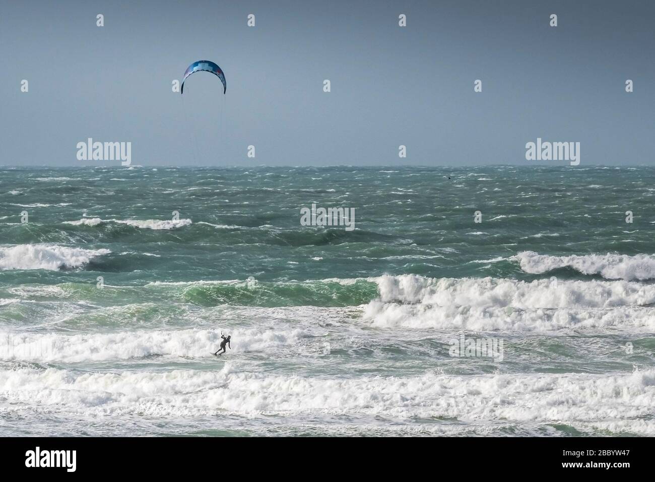 Un surfeur de kite solitaire bravant les conditions venteuses sauvages à Fistral, à Newquay, en Cornwall. Banque D'Images