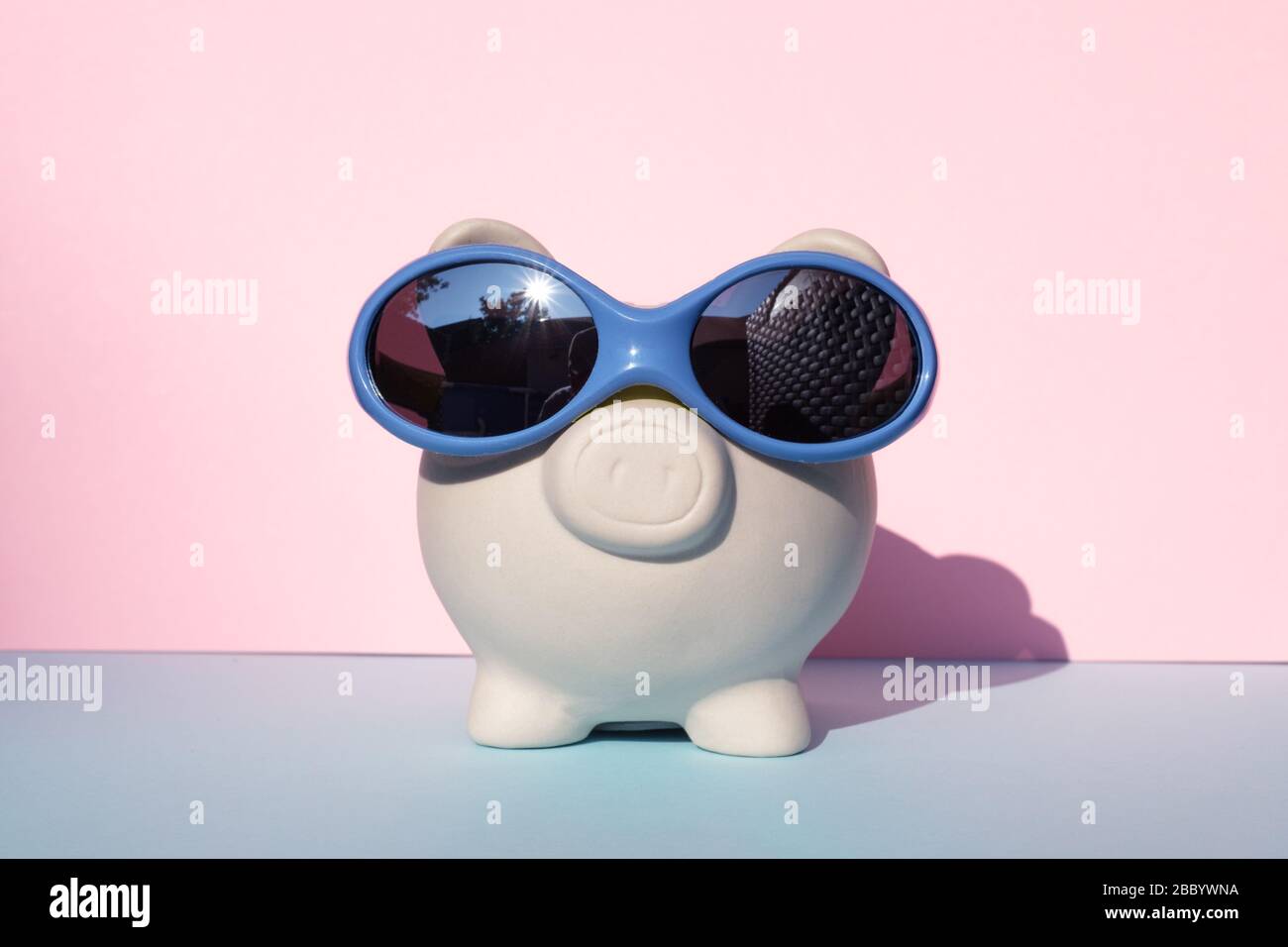 Porc moneybox blanc avec lunettes de soleil sur fond rose et bleu Banque D'Images