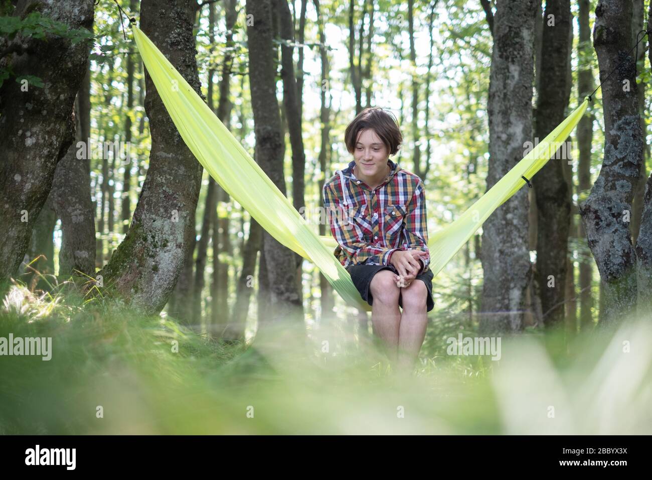 Joyeux garçon sur un hamac jaune dans la forêt de printemps. Concept de paysage de voyage. Camping en plein air Banque D'Images