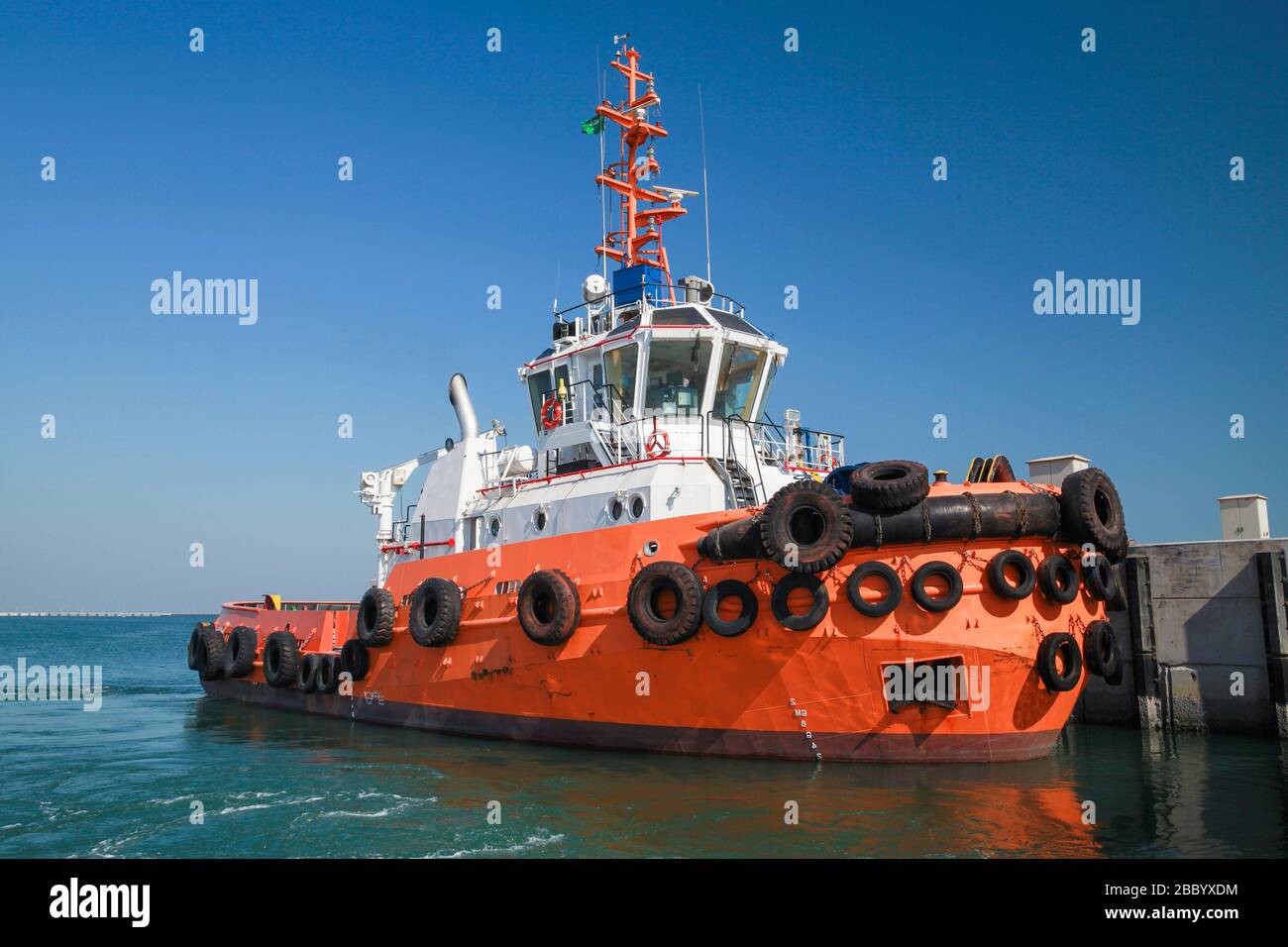 Un bateau remorqueur avec coque orange lumineuse est amarré dans un port Banque D'Images