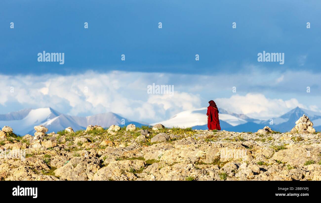 Femme, pèlerin bouddhiste en robe rouge marchant dans le désert. En arrière-plan montagnes du plateau tibétain. Près du lac Nam Co. Ciel spectaculaire Banque D'Images
