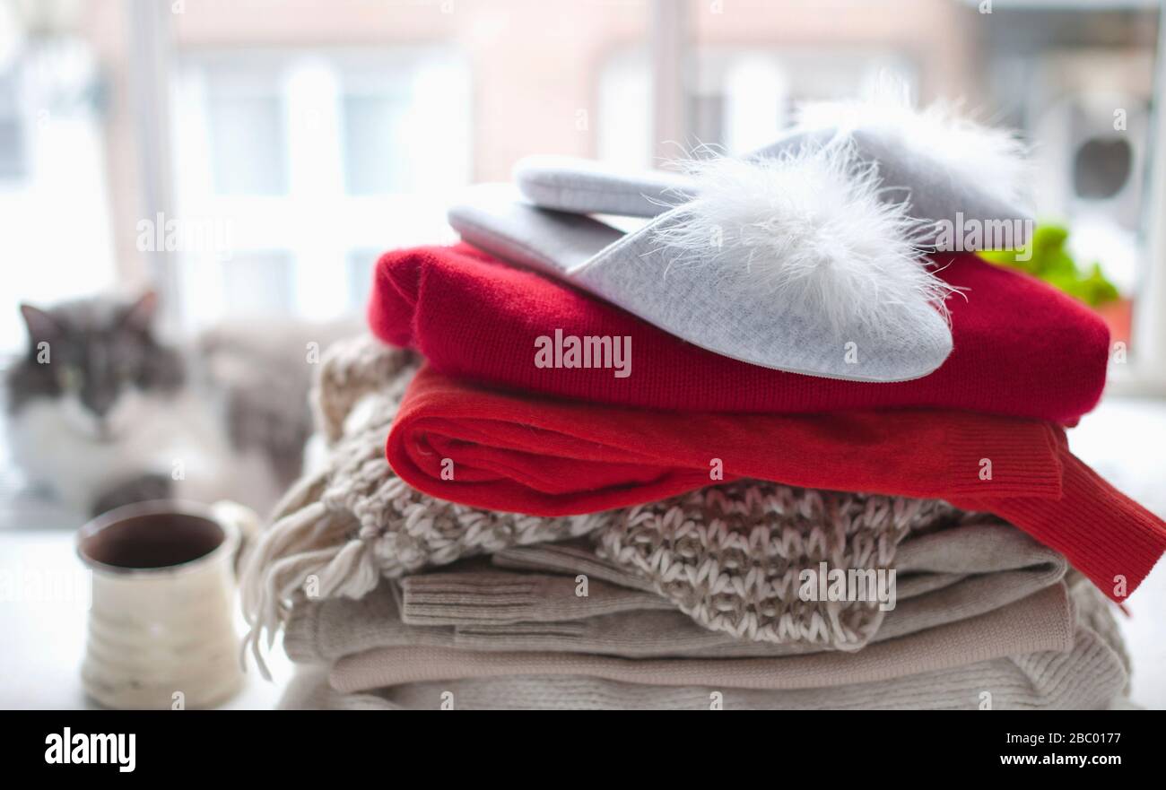 pile de sweaters tricotés confortables et de pantoufles hom. près de la grande fenêtre. En arrière-plan, un chat flou n'est plus concentré. PET et vêtements chauds. Concept automne-hiver. Espace de copie. Banque D'Images