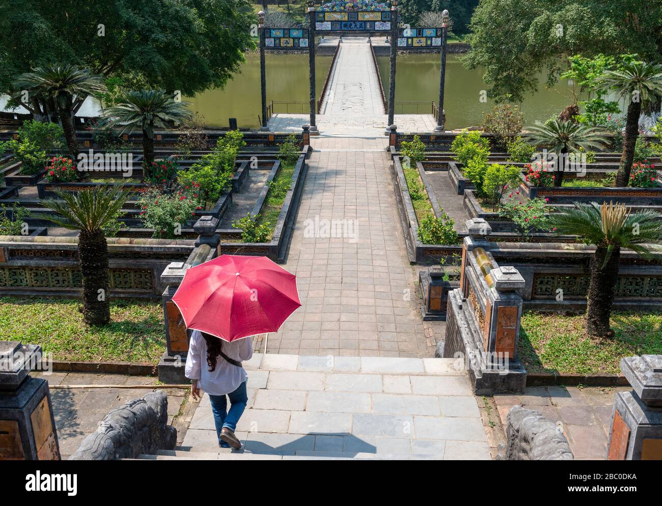 Dame vietnamienne avec parasol marchant vers le pont Trung Dao et la tombe de Minh Mang dans les jardins du complexe de la Citadelle impériale Hue, Vietnam Banque D'Images