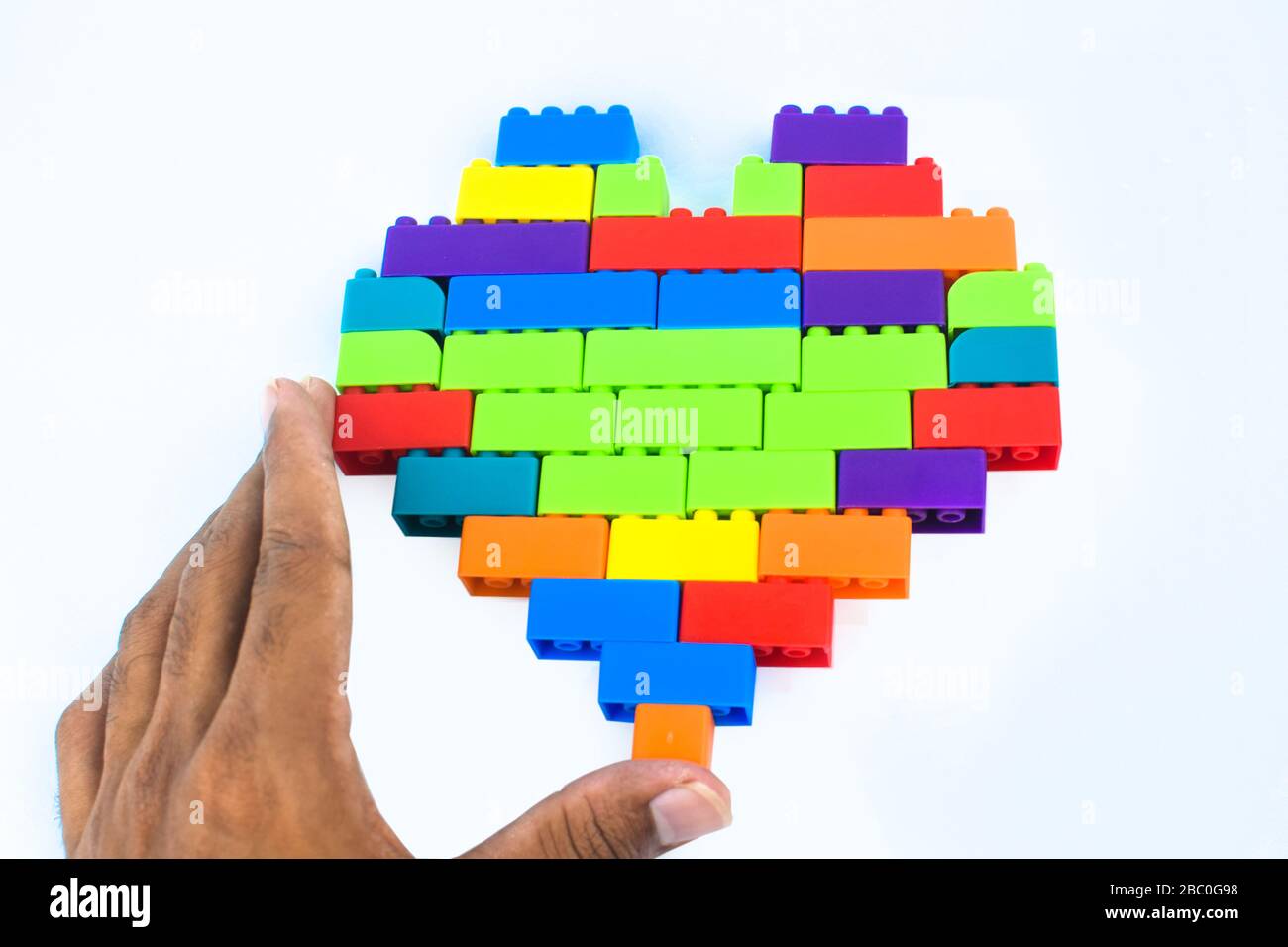 Une personne qui fait une forme de coeur avec beaucoup de différents blocs de construction de couleur devant un n arrière-plan blanc isolé Banque D'Images