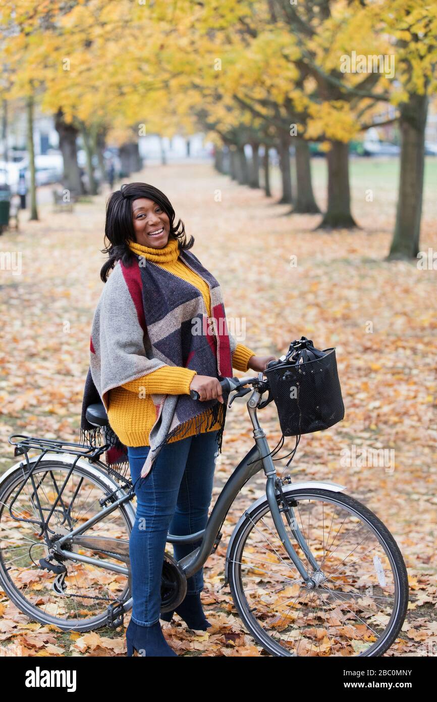 Portrait souriant, femme confiante de faire du vélo parmi les arbres et les feuilles dans le parc d'automne Banque D'Images