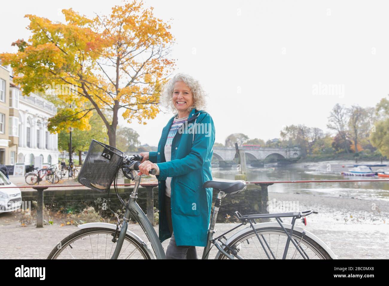 Portrait souriant femme senior vélo équitation le long de la rivière d'automne Banque D'Images