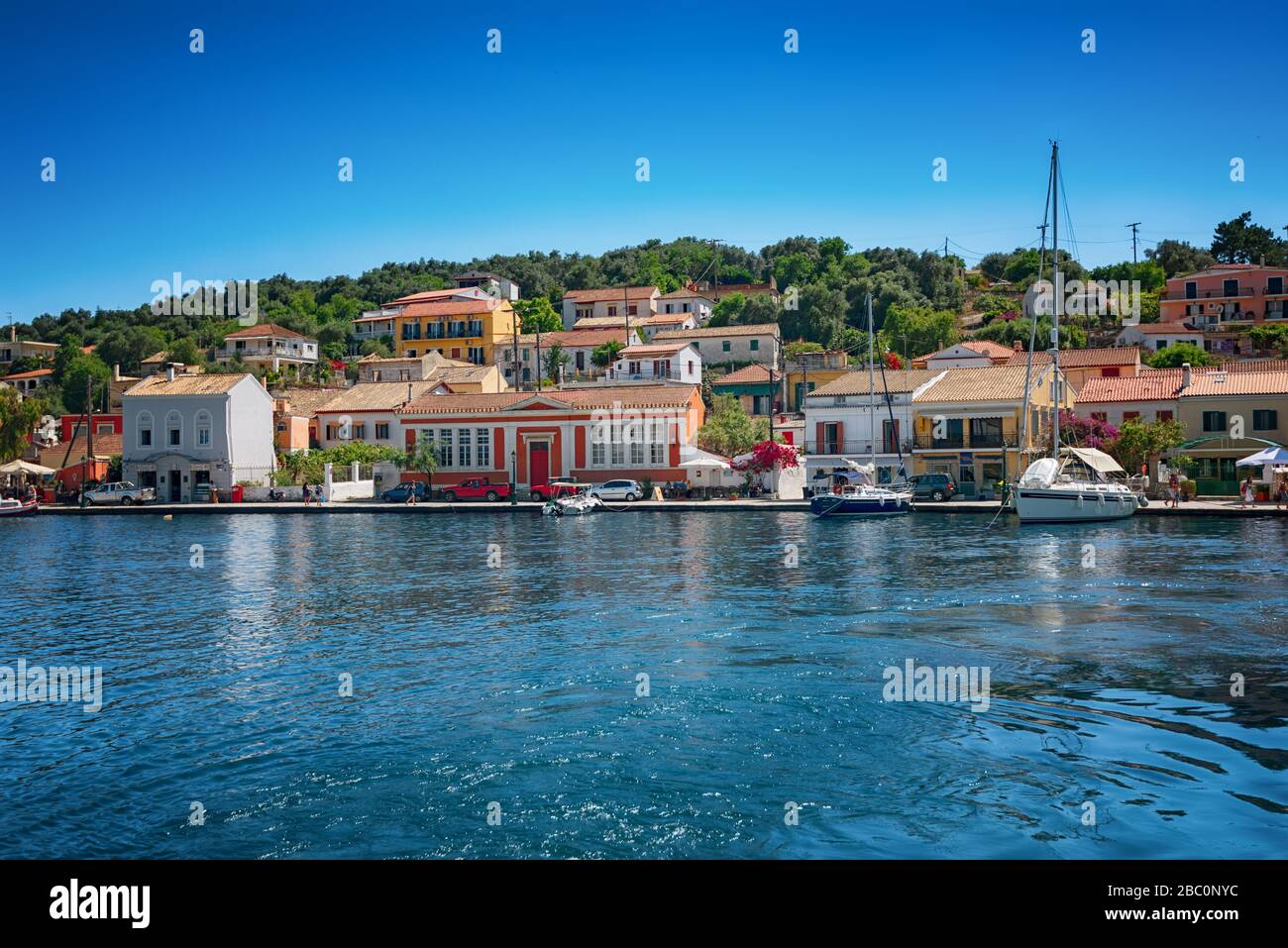 Île Paxos, Grèce. Vue sur la magnifique baie de la mer du port de Loggos avec de l'eau turquoise calme, bateaux et yachts vieilles maisons colorées et ciel bleu avec blanc Banque D'Images