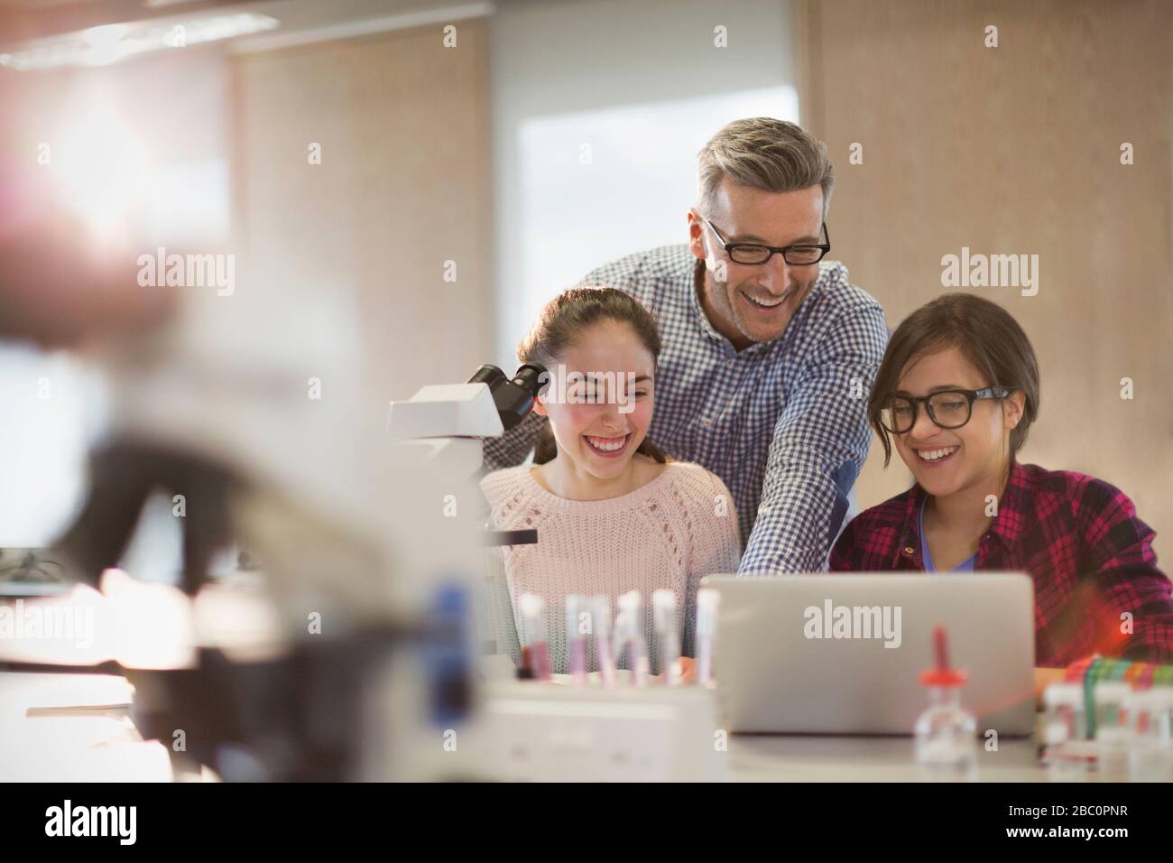 Professeur de sexe masculin et jeune fille qui mènent des expériences scientifiques au microscope et à l'ordinateur portable en salle de classe de laboratoire Banque D'Images