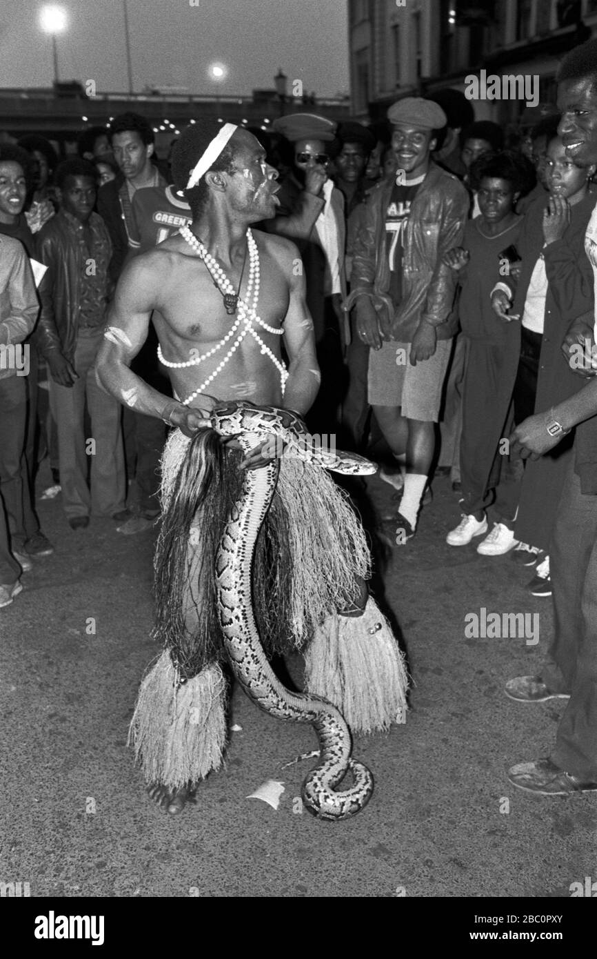 Notting Hill Carnival homme vêtu de "costume africain noir avec serpent vivant divertissant une foule de goers de carnaval. 1980 ROYAUME-UNI 1981 HOMER SYKES Banque D'Images