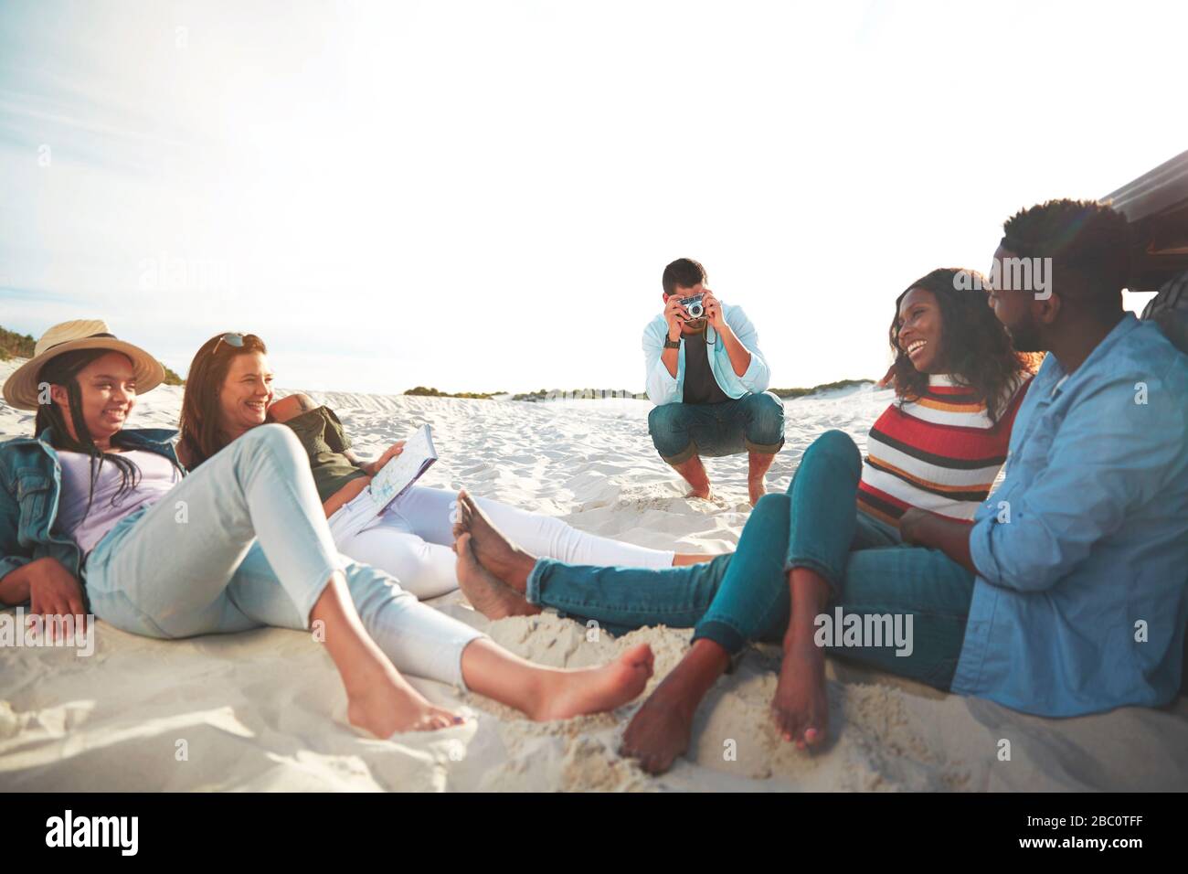 Jeune homme avec appareil photo numérique photographier des amis se détendre sur la plage Banque D'Images