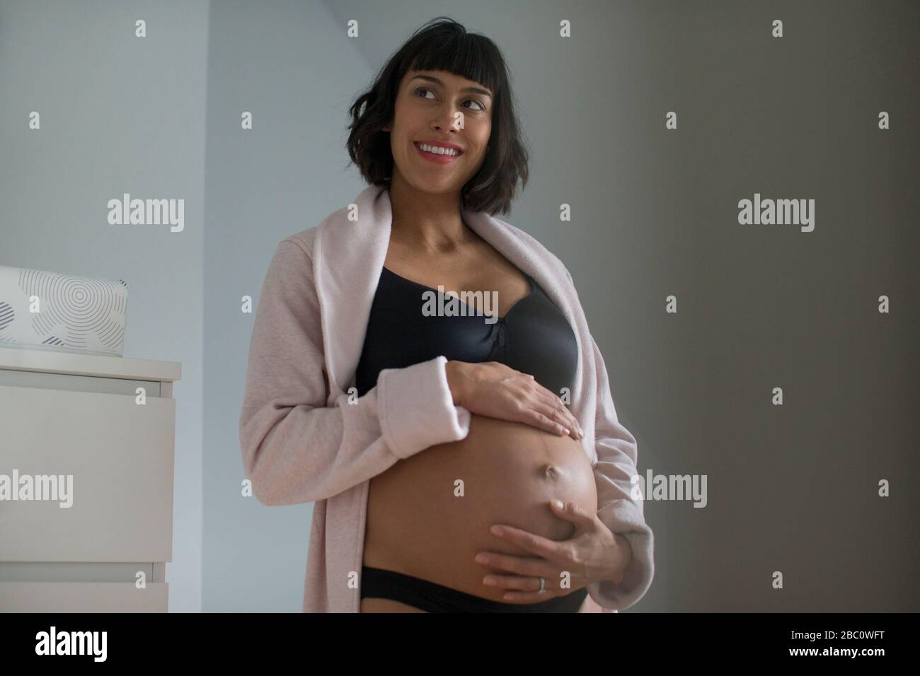 Bonne femme enceinte dans peignoir et soutien-gorge tenant l'estomac Banque D'Images