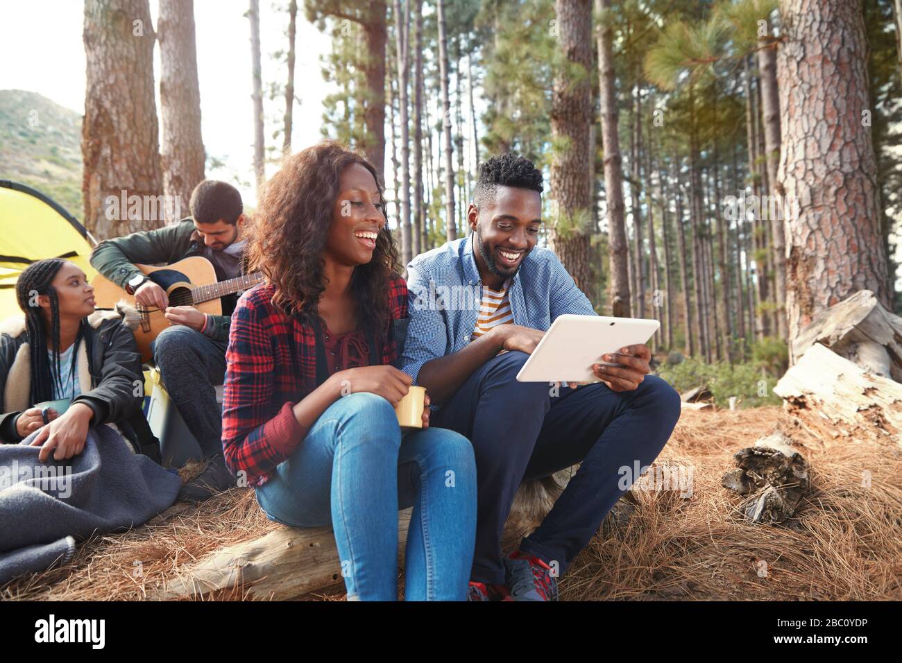 Jeune couple souriant utilisant une tablette numérique au camping dans les bois Banque D'Images