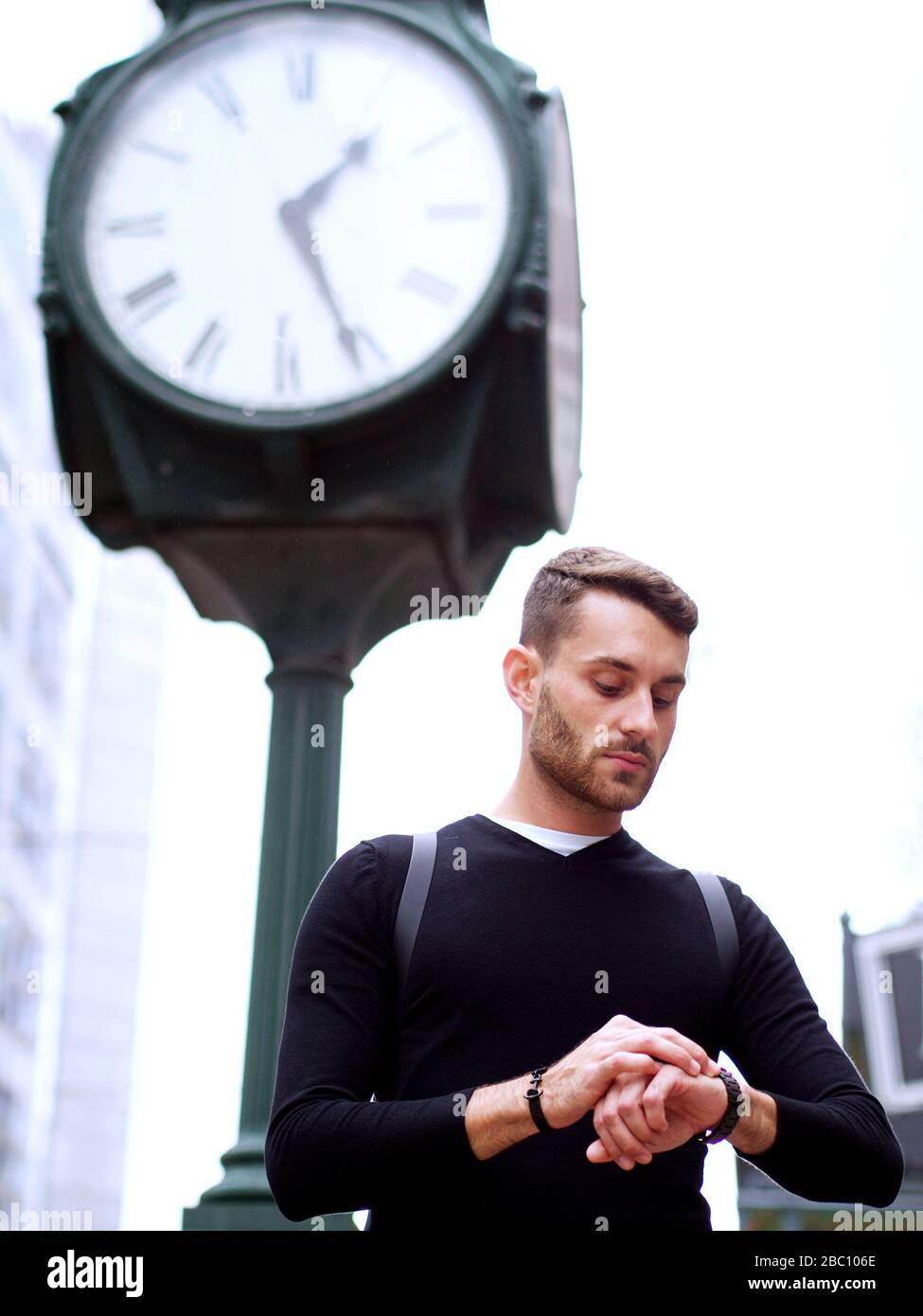 Homme d'affaires inquiet se tenant sous l'horloge de la ville dans un centre-ville regardant son montre de poignet, concept d'une gestion du temps et de l'exploitation de la douleur. Banque D'Images