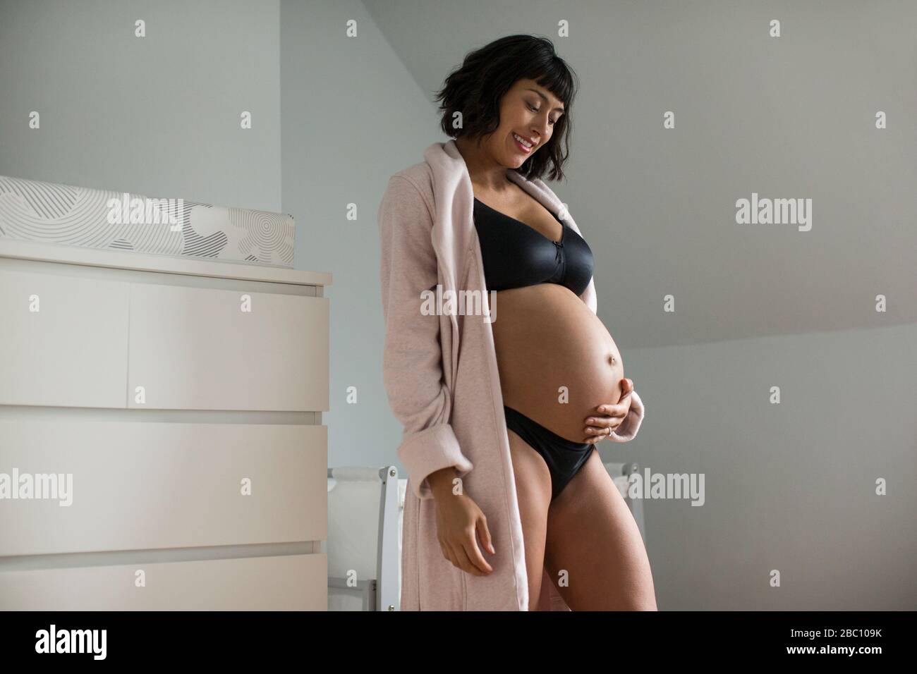 Bonne belle femme enceinte dans le soutien-gorge et peignoir tenant l'estomac Banque D'Images
