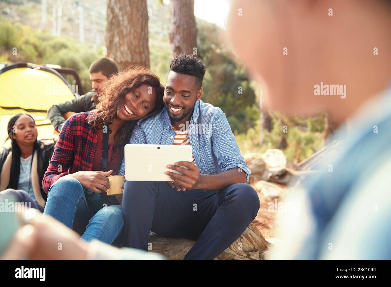 Jeune couple souriant utilisant une tablette numérique au camping Banque D'Images