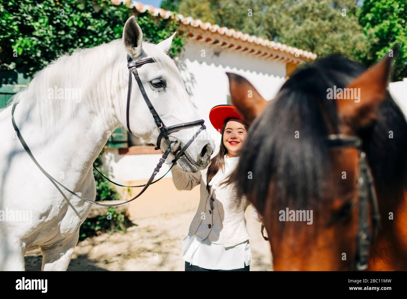 Adolescent avec syndrome de Down portant un chapeau rouge avec deux chevaux Banque D'Images